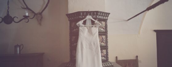 Weißes Brautkleid von Julia hängt an einem verziertem Holzrahmen in einem rustikalen Zimmer des Schloss Ernegg – Mittelalter-Schloss Atmosphäre