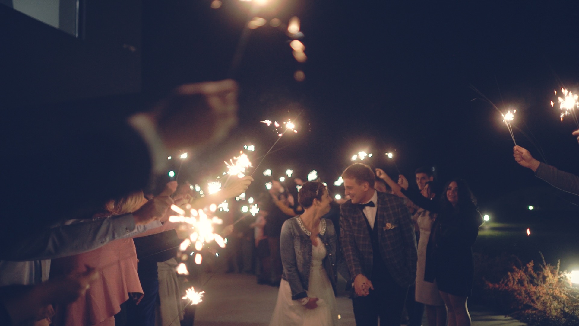 Bius és Csabi az esküvői vendégek között éjszakában a Kreinbacher birtok udvarán, világítóanyagok és fények körülötte