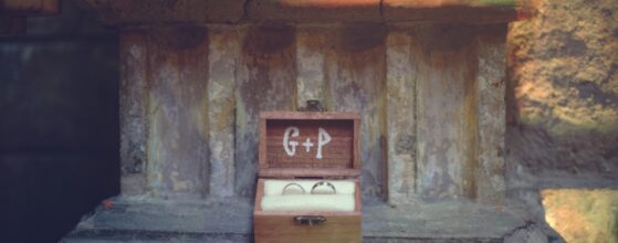 Wedding rings of Gabi and Phil in a small wooden ring box with the initials G + P, placed on a stone ledge at BrodyLand The Studios in Budapest