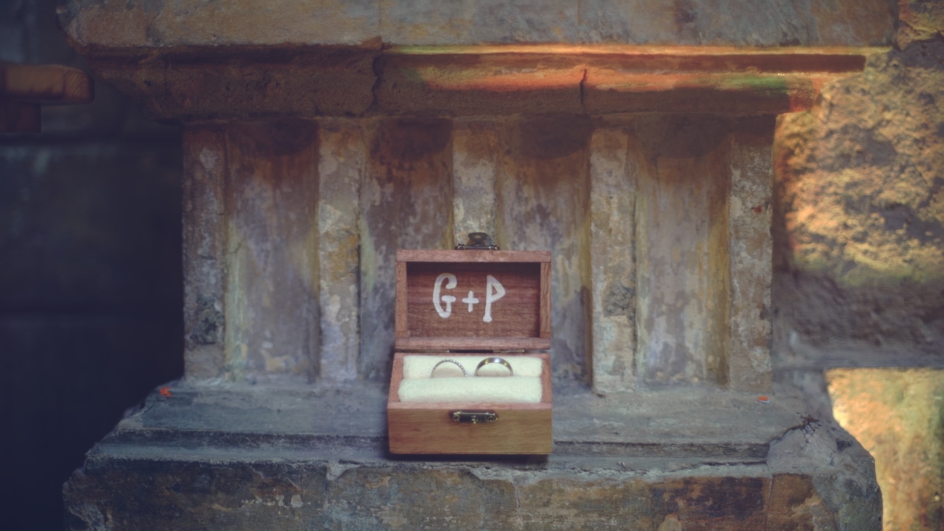 Wedding rings of Gabi and Phil in a small wooden ring box with the initials G + P, placed on a stone ledge at BrodyLand The Studios in Budapest