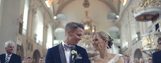 Eva und Patrik stehen während der Trauung in der festlich geschmückten Kirche in Matrei in Osttirol, im Hintergrund Deckenfresken und Orgel