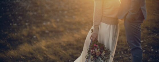 Dóri és Ákos állnak egymás felé fordulva a naplementében, a menyasszony kezében laza, színes csokor – egy meleg, őszi pillanat az esküvői filmjükből.