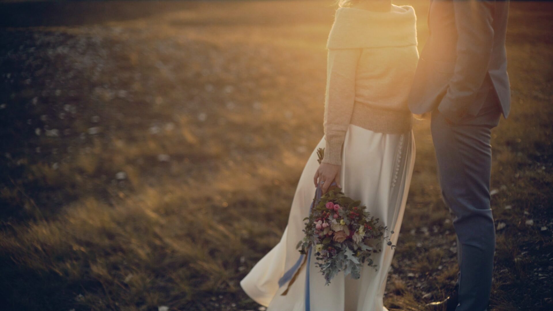 Dóri és Ákos állnak egymás felé fordulva a naplementében, a menyasszony kezében laza, színes csokor – egy meleg, őszi pillanat az esküvői filmjükből.