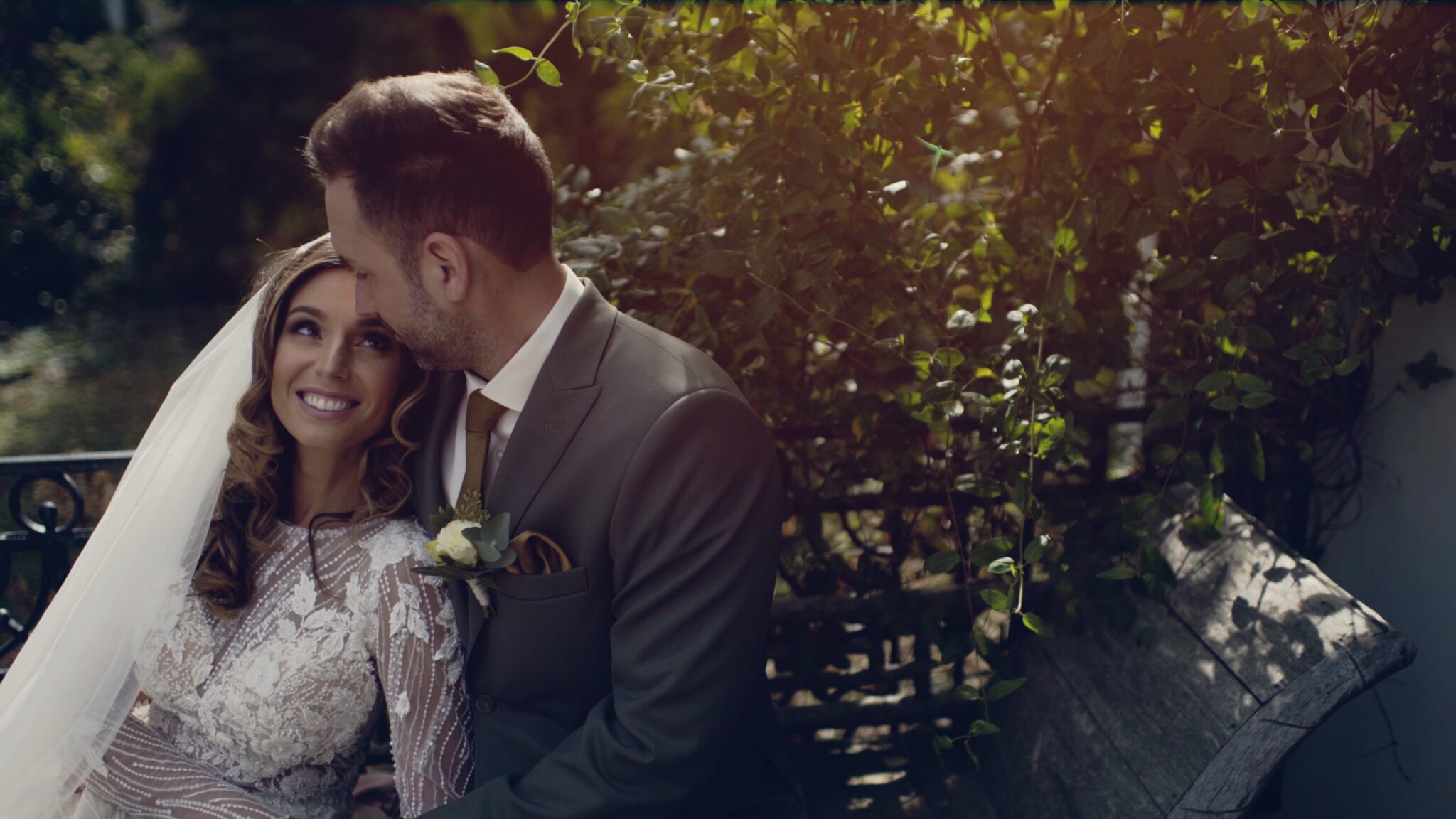 Laura és Bence egy romantikus kertben ülnek egymás mellett, elegáns magyar luxus esküvőjükön, lágy napfényben – egy intim pillanat az esküvői filmből.