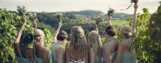 Jessica und ihre Brautjungfern stehen im Weingarten beim Holler Weingut Scheune und heben ihre Sträuße in die Luft – ein sommerlicher Moment aus ihrem Hochzeitsfilm.