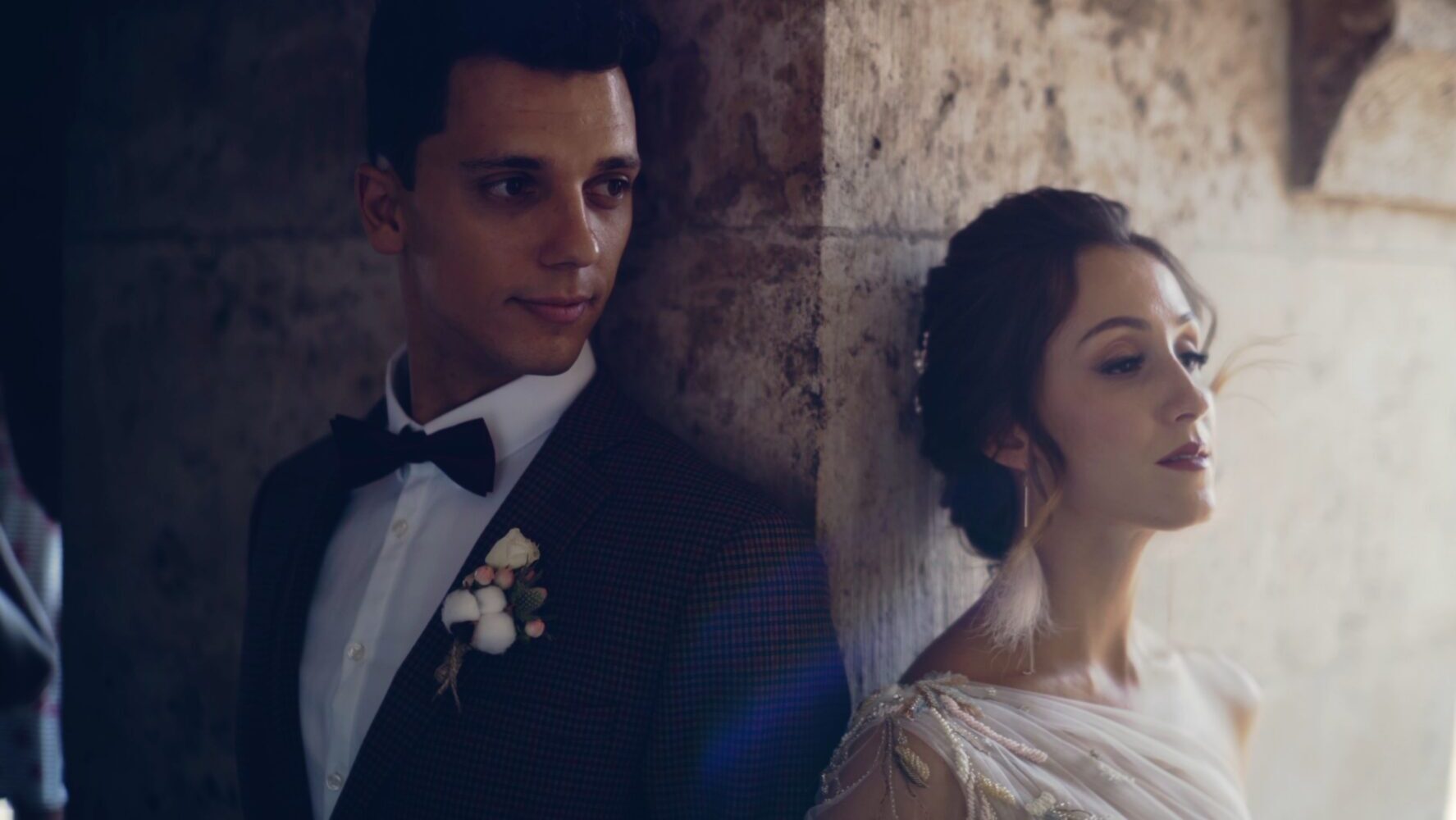 Nadya and Tomi leaning against the stone wall at Event’s Hill in Budapest, half in shadow and half in sunlight – a cinematic portrait from their Russian-Hungarian wedding film.