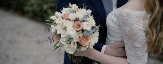 Stephanie und Paul stehen eng umarmt beim Pfarrwirt in Wien, der Brautstrauß mit zarten Pastellblumen ist im Vordergrund – ein stilles Detail aus ihrem Hochzeitsfilm.