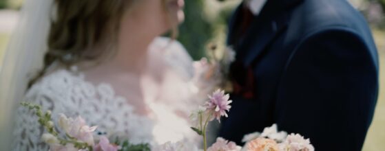 Kinga and Neal leaning close to each other behind a bouquet of soft pastel flowers at Tópart Hotel in Balatonvilágos – a romantic moment from their Lake Balaton wedding film.