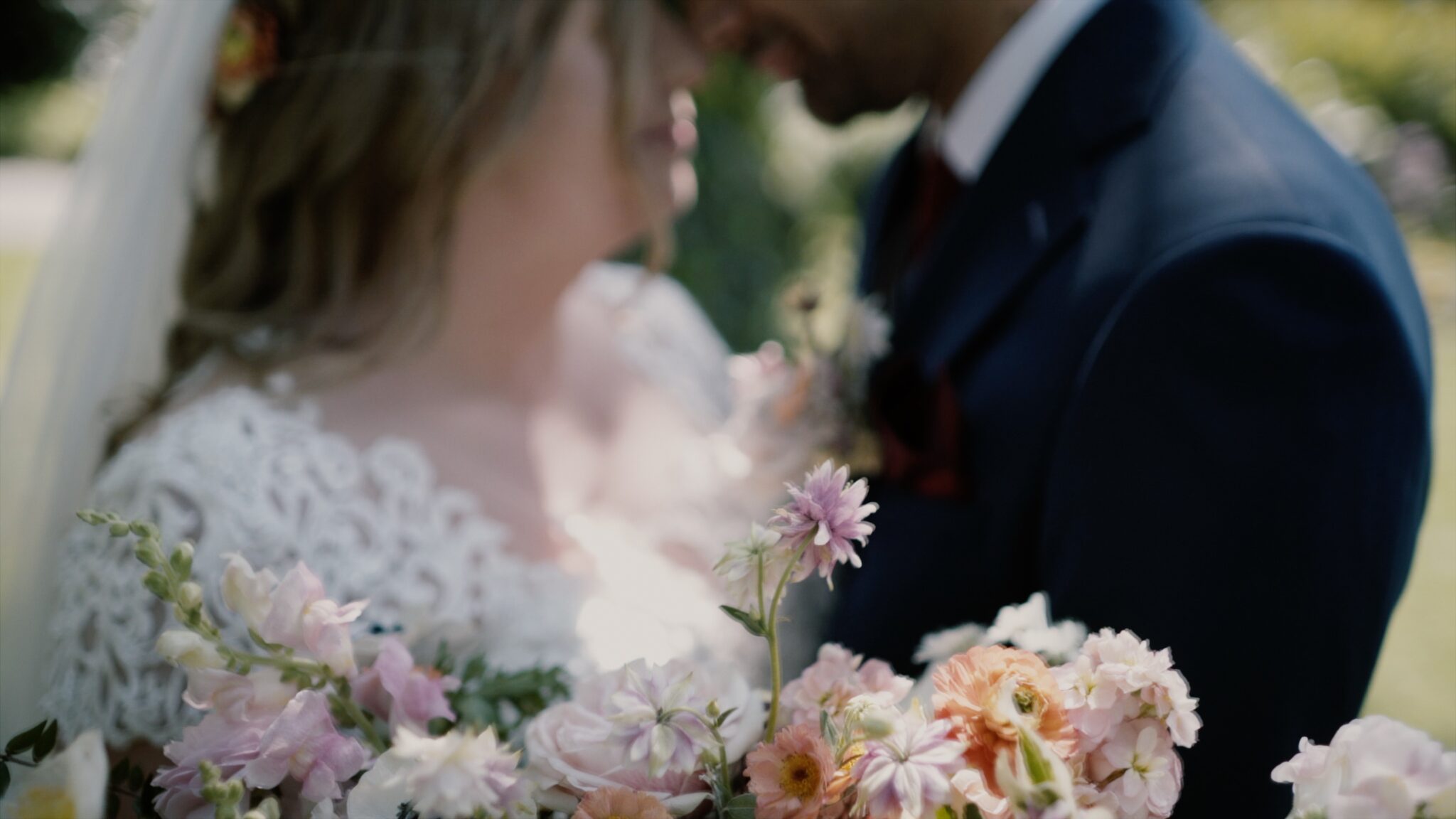 Kinga and Neal leaning close to each other behind a bouquet of soft pastel flowers at Tópart Hotel in Balatonvilágos – a romantic moment from their Lake Balaton wedding film.