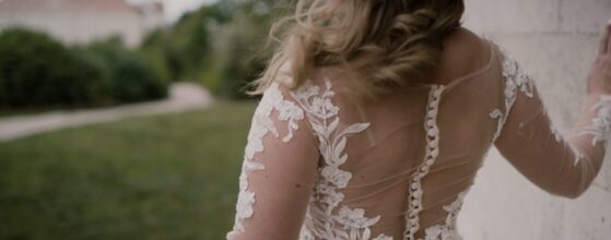 Szandra csipkés hátú menyasszonyi ruhában áll a pannonhalmi dombok között, finoman megérinti a falat – egy elegáns részlet az esküvői filmből. Pannonhalma esküvői film CulinArt