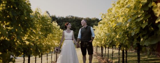 Alexandra und Christopher Hand in Hand zwischen den Reben beim Gustoplatzl in Klöch in der Steiermark – ein sonniger Moment aus ihrem Hochzeitsfilm. Gustoplatzl Hochzeit videograf