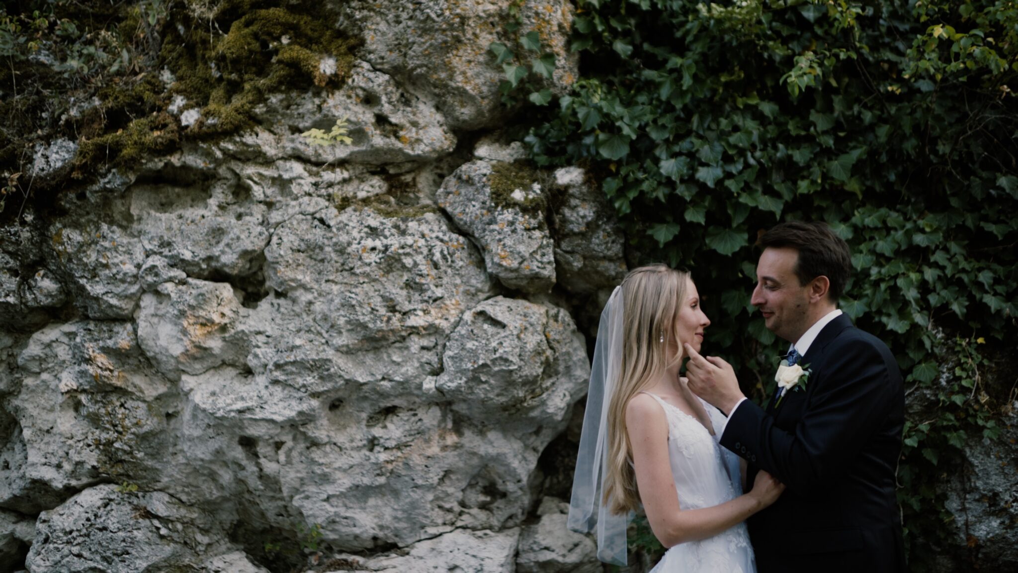 Anita és Ádám a tihanyi Echo étterem sziklái előtt állnak egymáshoz közel, háttérben a Balaton-parti sziklafal – egy meghitt pillanat a tihanyi esküvői filmjükből.