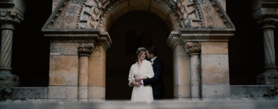 Orsi és Gábor a Vajdahunyadvár boltívei alatt állnak Budapest téli fényében, összebújva – egy különleges, hideg évszakos pillanat az esküvői filmjükből.