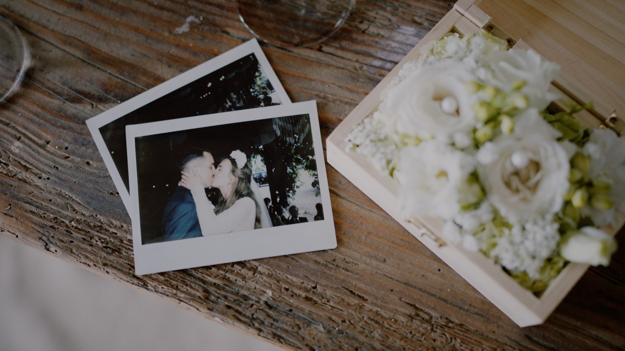 Zwei Polaroid-Fotos von Diana und Alex liegen auf einem Holztisch neben einer Blumenbox – ein verspieltes Detail ihres Hochzeitsfilms im Weingut Holler in Spielfeld.