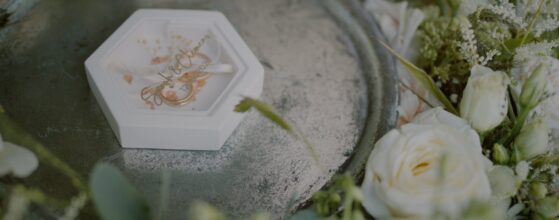 Die Eheringe von Sarah und Clemens liegen in einer eleganten Box auf einem Tablett, umgeben von Blumen – ein liebevolles Detail ihres Hochzeitsfilms im Der Oberhauser in Holzhausen.