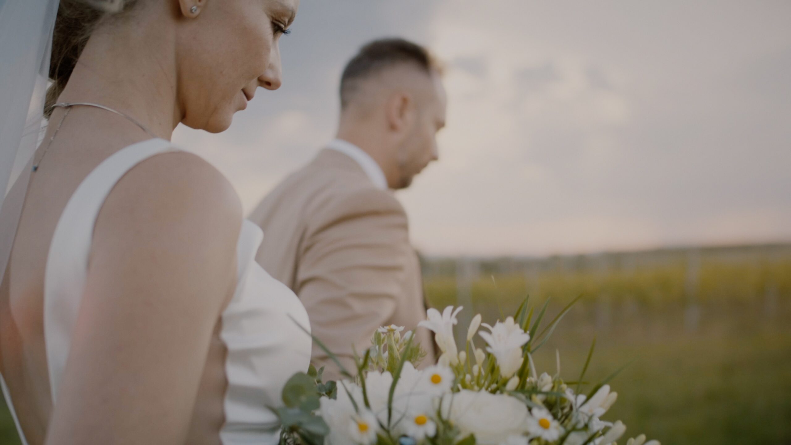 Bride holding a white and green bouquet while walking with the groom between the vineyards at Rókusfalvy Birtok in Etyek – detail from Móni and Levi’s wedding film.