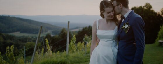 Bride and groom standing on the hill above the vineyards at Weingartenhotel Harkamp in St. Nikolai im Sausal, with the Styrian landscape in the background – scene from their wedding film.”