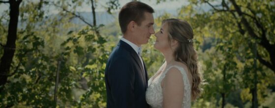 Carina und Werner stehen sich im Weingarten bei der Holler Scheune in Spielfeld gegenüber und lächeln sich an – ruhiger Moment aus ihrem Hochzeitsfilm.