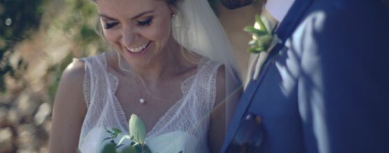 Annie hält ihren Eukalyptus-Brautstrauß, während Chris in seinem blauen Anzug lächelnd neben ihr steht bei ihrer Hochzeit in Algarve bei Albufeira Portugal wedding videographer