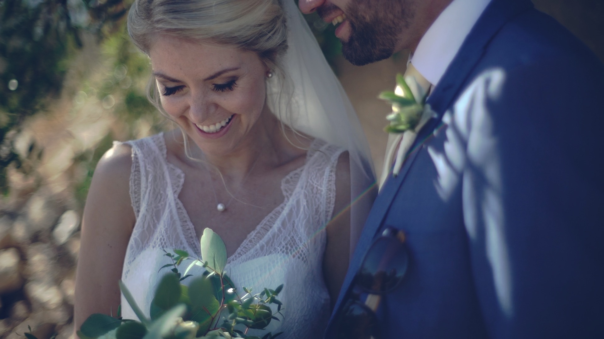 Annie hält ihren Eukalyptus-Brautstrauß, während Chris in seinem blauen Anzug lächelnd neben ihr steht bei ihrer Hochzeit in Algarve bei Albufeira Portugal wedding videographer