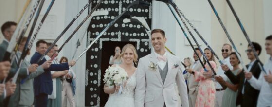 Carina und Christoph gehen nach der Trauung Hand in Hand aus der Kirche, während Freunde mit Eishockeyschlägern ein Ehrenspalier bilden – Hochzeitsfilm im Liszt Weingut in Leithaprodersdorf.
