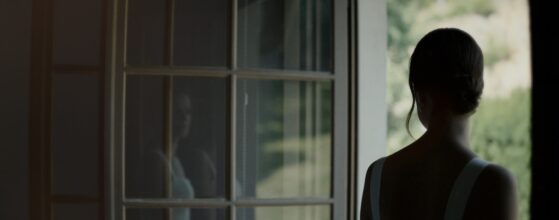 Christina steht im Fensterlicht im Lorenz Wachau in Leiben, ihre Silhouette spiegelt sich in der Glasscheibe – ruhiger Moment im Hochzeitsfilm.