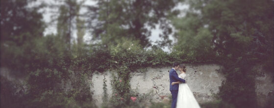 Braut Daniela und Bräutigam Christian umarmen sich romantisch vor der historischen Steinmauer des Schloss Walpersdorf Parks – aus ihrem Hochzeitsteaser