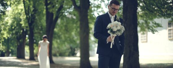 Emotionales Hochzeitsvideo Schloss Halbturn Bräutigam René hält den Brautstrauß in einer Baumallee im Park des Schlosses Halbturn, während Braut Daniela von hinten näher kommt für ihren First Look