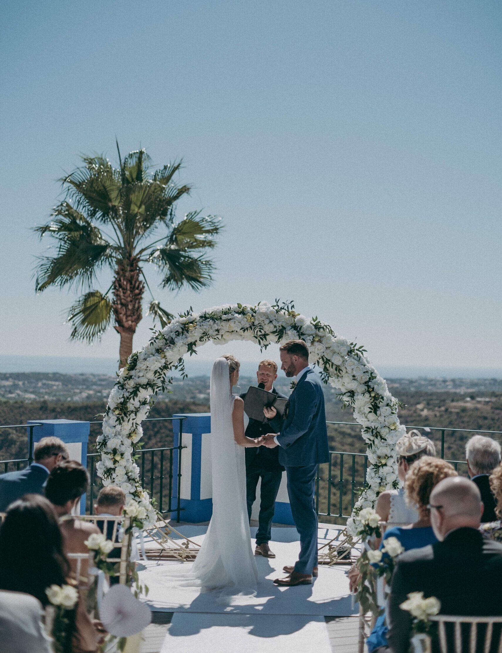 Outdoor destination wedding ceremony in Albufeira, Portugal, with a couple standing under a floral arch overlooking the sea, filmed by a destination wedding videographer in Europe.