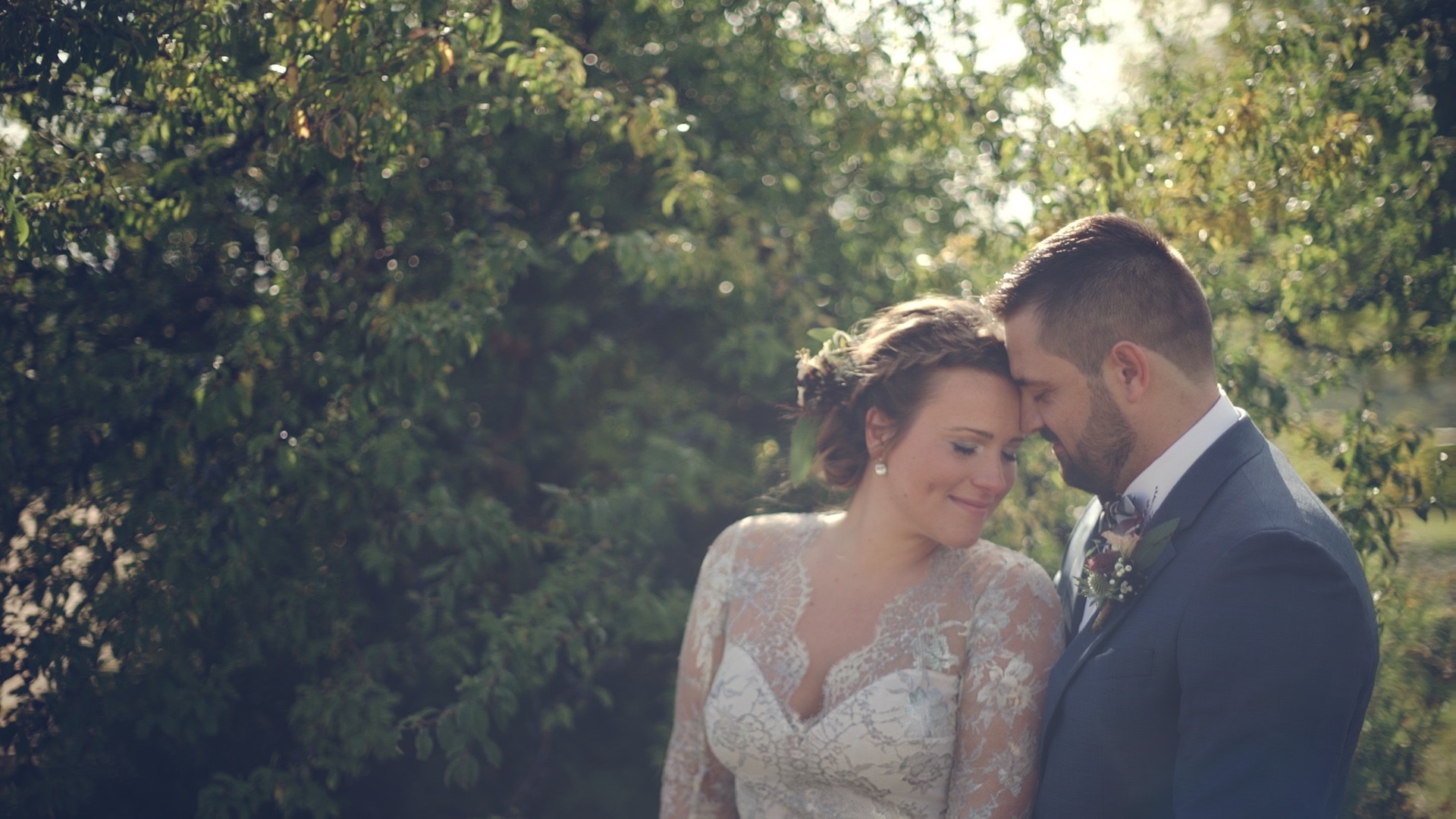 Hilltop Borbirtok esküvő Dóri és Csani az esküvői képen a szőlőültetvény között, Dóri fehér csipke ruhájában és Csani kék öltönyében, aranyos napfénnyel körülöttük