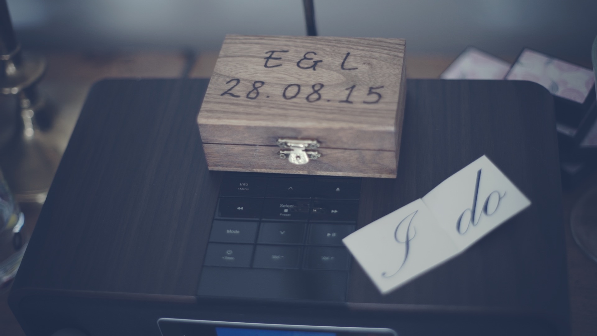 Wooden ring box with Em and Liam’s wedding date and a small card saying I do at Old Swan and Minster Mill, a soft, intimate wedding detail from their film in England.