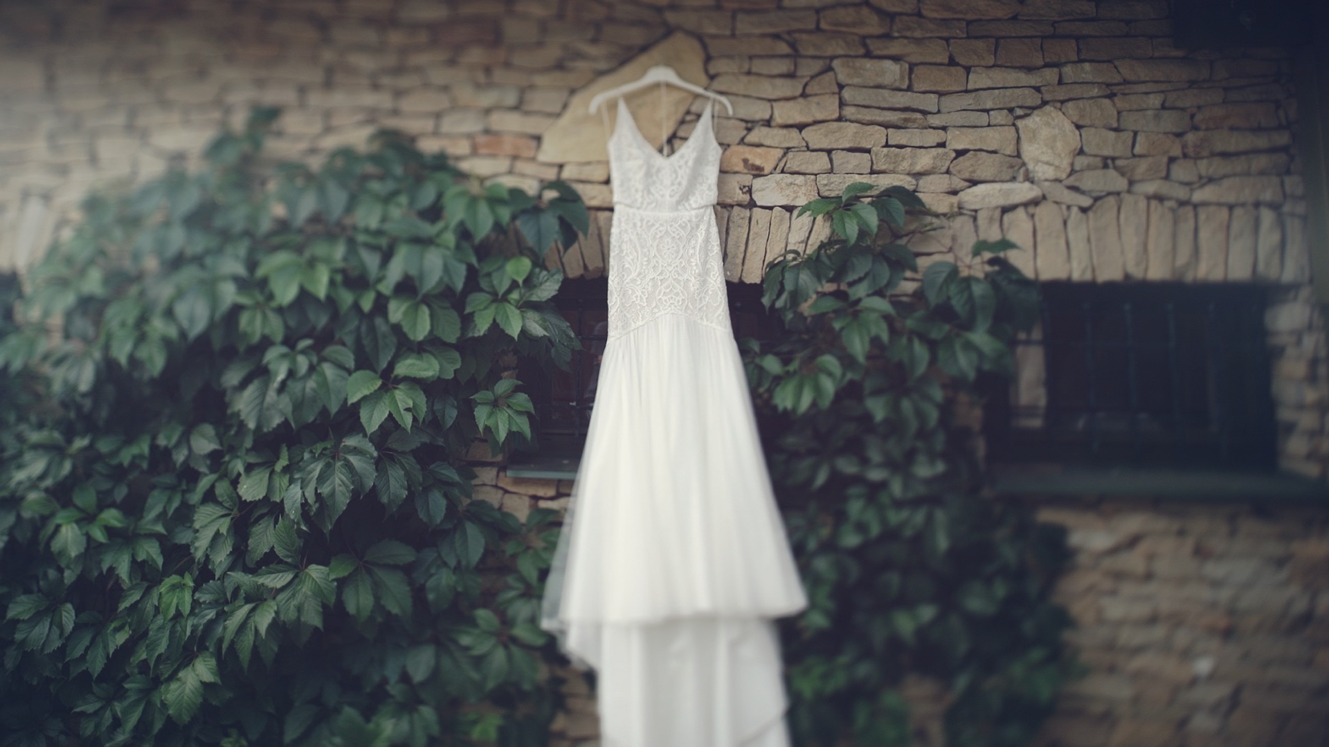 Talléros rendezvényhaz Nyirtass esküvő Emőke menyasszonyi ruhájában függőleges helyzetben a Talléros rendezvényhá falánál, zöld borostyánokkal övezve, esküvői film részlet