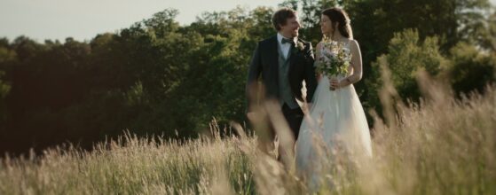 Evi und Florian gehen Hand in Hand durch eine Wiese am Am Roan bei Wien, festgehalten im weichen Abendlicht ihres Hochzeitsfilms.