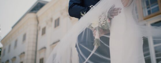 Der Schleier weht im Wind, während Julia und Stefan sich vor Schloss Halbturn im Burgenland umarmen – ein leichter, sommerlicher Moment aus ihrem Hochzeitsfilm.