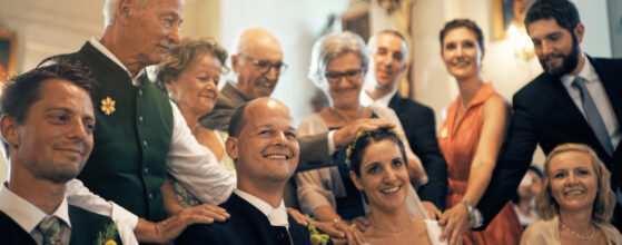 Familie und Freunde legen ihre Hände auf das Brautpaar Katharina und Martin während einer Segnung in der Kirche bei ihrer Hochzeit in Spielfeld Hochzeitsvideograf Schloss Spielfeld Weingut