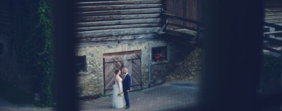 Kirsti in weißem Brautkleid und Florian im dunklen Anzug umarmen sich romantisch unter einem eleganten Bogen im historischen Weitmoser Schlössl Bad Gastein