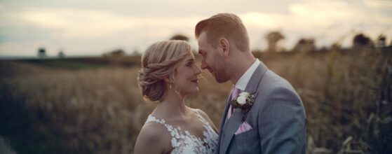 Lisa und Philip stehen eng umschlungen auf einem Feld in der Nähe von Schloss Halbturn, im weichen Abendlicht – ein romantischer Moment aus ihrem Hochzeitsteaser.