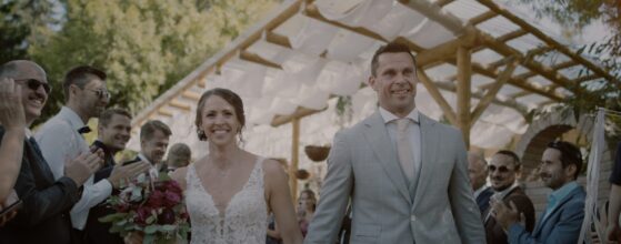 Manu und Armin gehen nach der freien Trauung zwischen ihren Gästen hindurch im Winzerhotel Kolleritsch, alle klatschen und feiern – ein fröhlicher Moment aus ihrem Hochzeitsfilm. Steiermark Weinberg Hochzeitsfilm