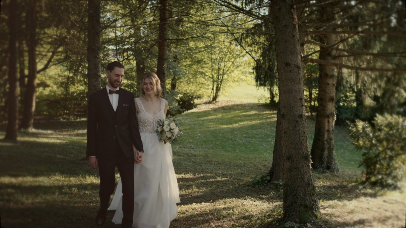 Marie und Lukas gehen Hand in Hand durch den Waldweg beim Winzerhotel Kolleritsch in der Steiermark, weiches Licht zwischen den Bäumen – eine ruhige Szene ihres Hochzeitsfilms.