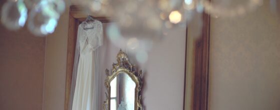 Das Hochzeitskleid von Nina hängt vor dem Spiegel im Zimmer des Schlosses Obermayerhofen, darüber funkelt ein Kronleuchter Schloss Obermayerhofen Hochzeit