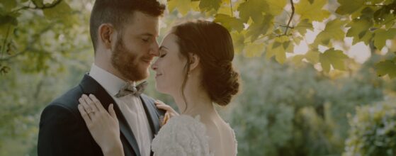 rsi és Bence ölelkeznek az Öreg Tölgy Kastély kertjében, a nyári napfényben – egy meghitt pillanat az esküvői filmből.