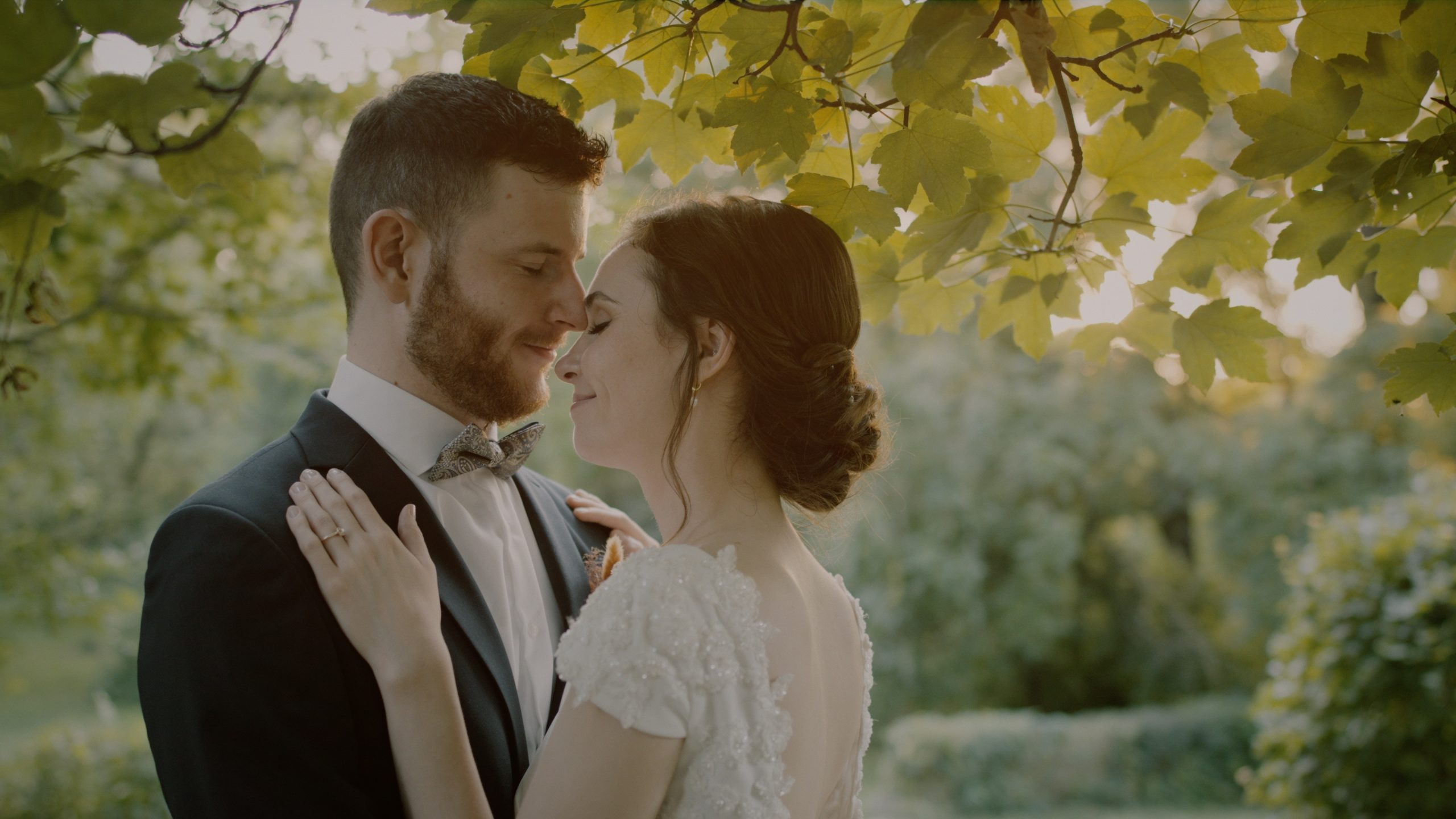 rsi és Bence ölelkeznek az Öreg Tölgy Kastély kertjében, a nyári napfényben – egy meghitt pillanat az esküvői filmből.