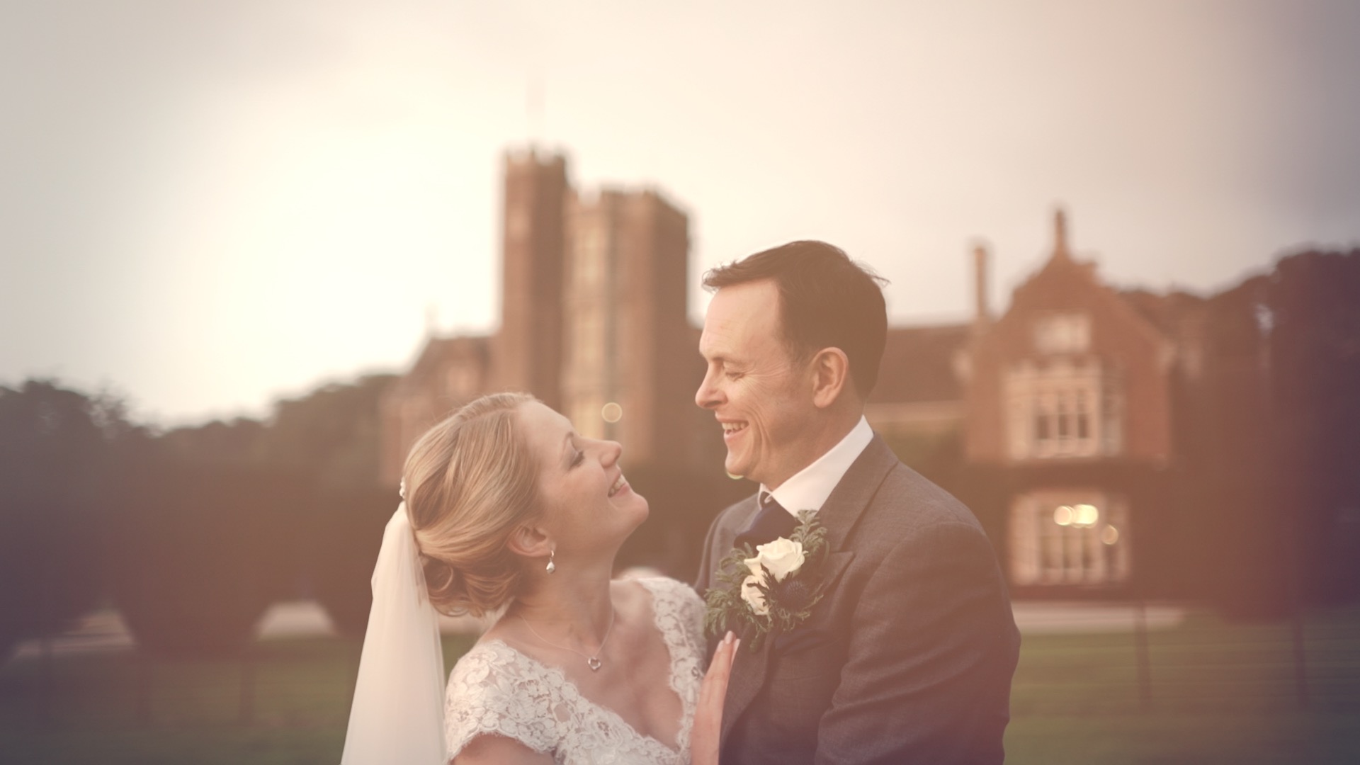 Soft evening portrait of Paula and James in front of St Audries Park in Somerset, England, with warm pastel light and a romantic wedding videography feel.