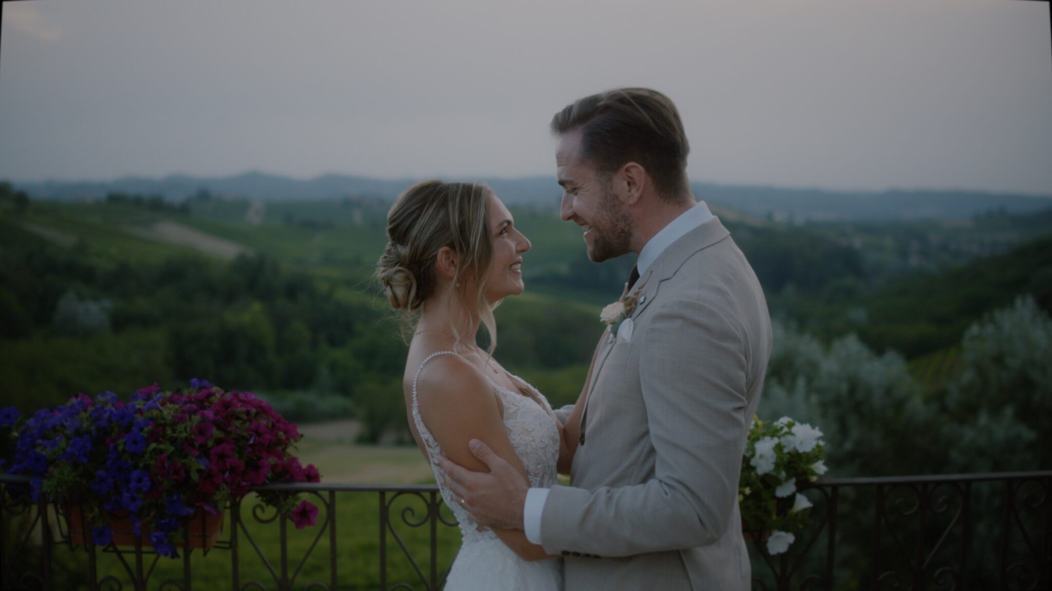 Rahel and William standing on the terrace of La Villa Hotel in Piemonte, looking at each other with rolling green hills at sunset in the background