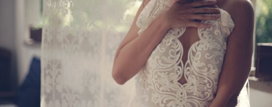 Timi a Nomád Hotel hotelszobájában csipke részletekkel díszített fehér esküvői ruhájában, napfényes ablaknál