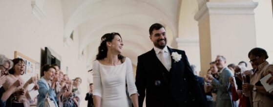 Victoria und Dominic gehen Hand in Hand durch den Ausgang der Kirche, umgeben von Gästen und Seifenblasen – ein fröhlicher Moment ihres Hochzeitsfilms bei Schloss Gurhof.