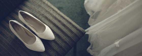 Hochzeitsvideograf Birkenhof Gols Burgenland Weingegend Weiße Brautenschuhe von Viktoria liegen auf einem dunklen Tuch neben ihrer fließenden Brautenrobe beim Birkenhof in Gols – elegantes Hochzeitsdetail