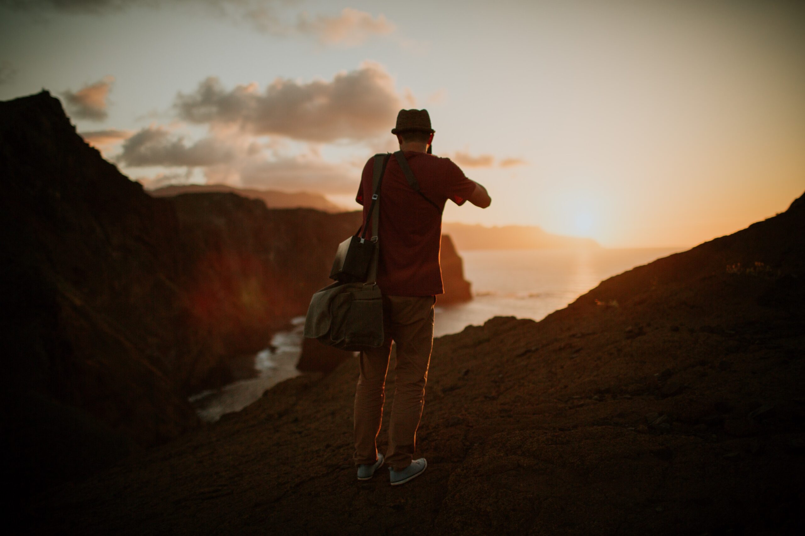 Wedding filmmaker Zsolt Barabas walking towards the sunset with camera bags on coastal cliffs