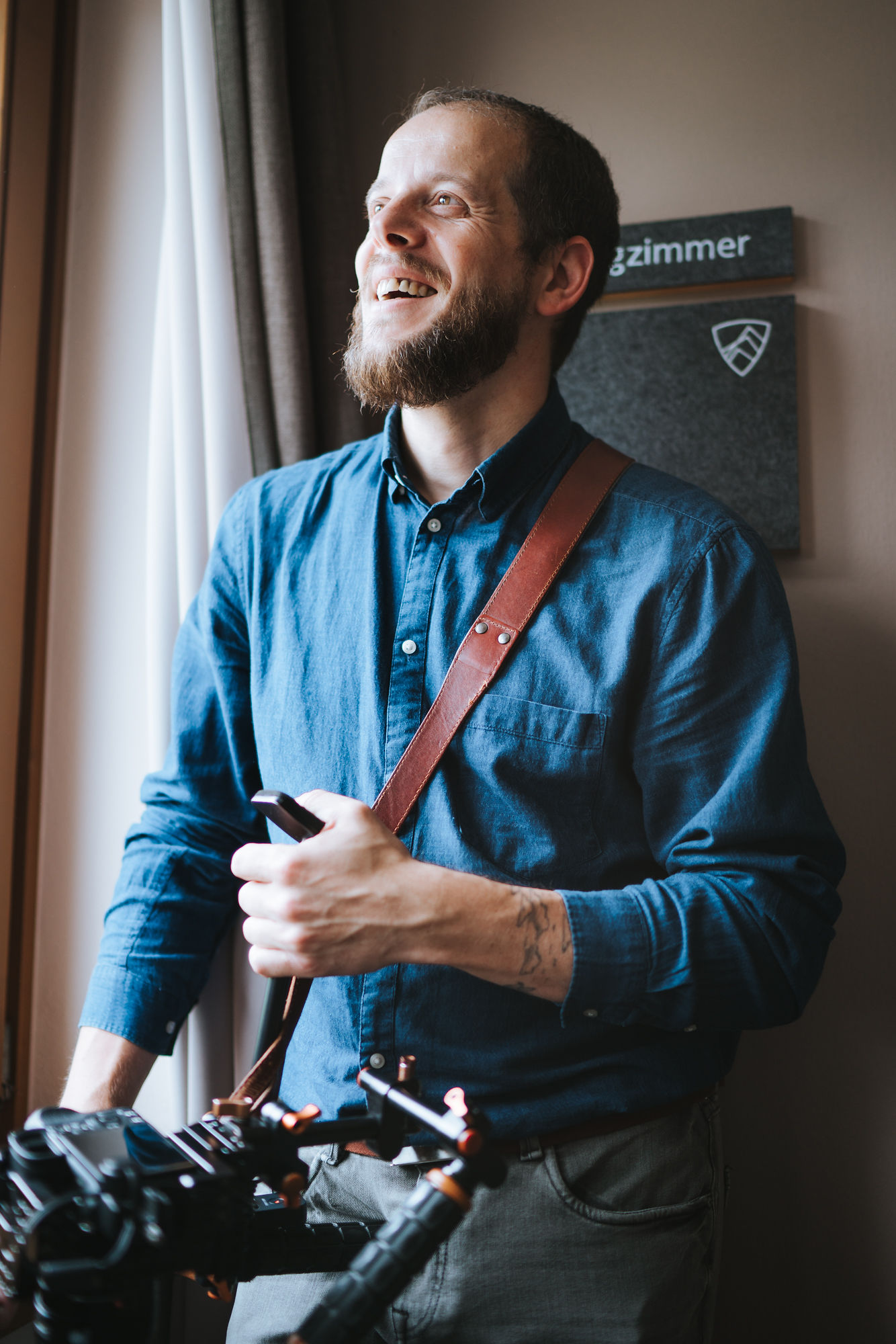 Wedding videographer Zsolt Barabas adjusting leather camera harness and gear by the window before a wedding