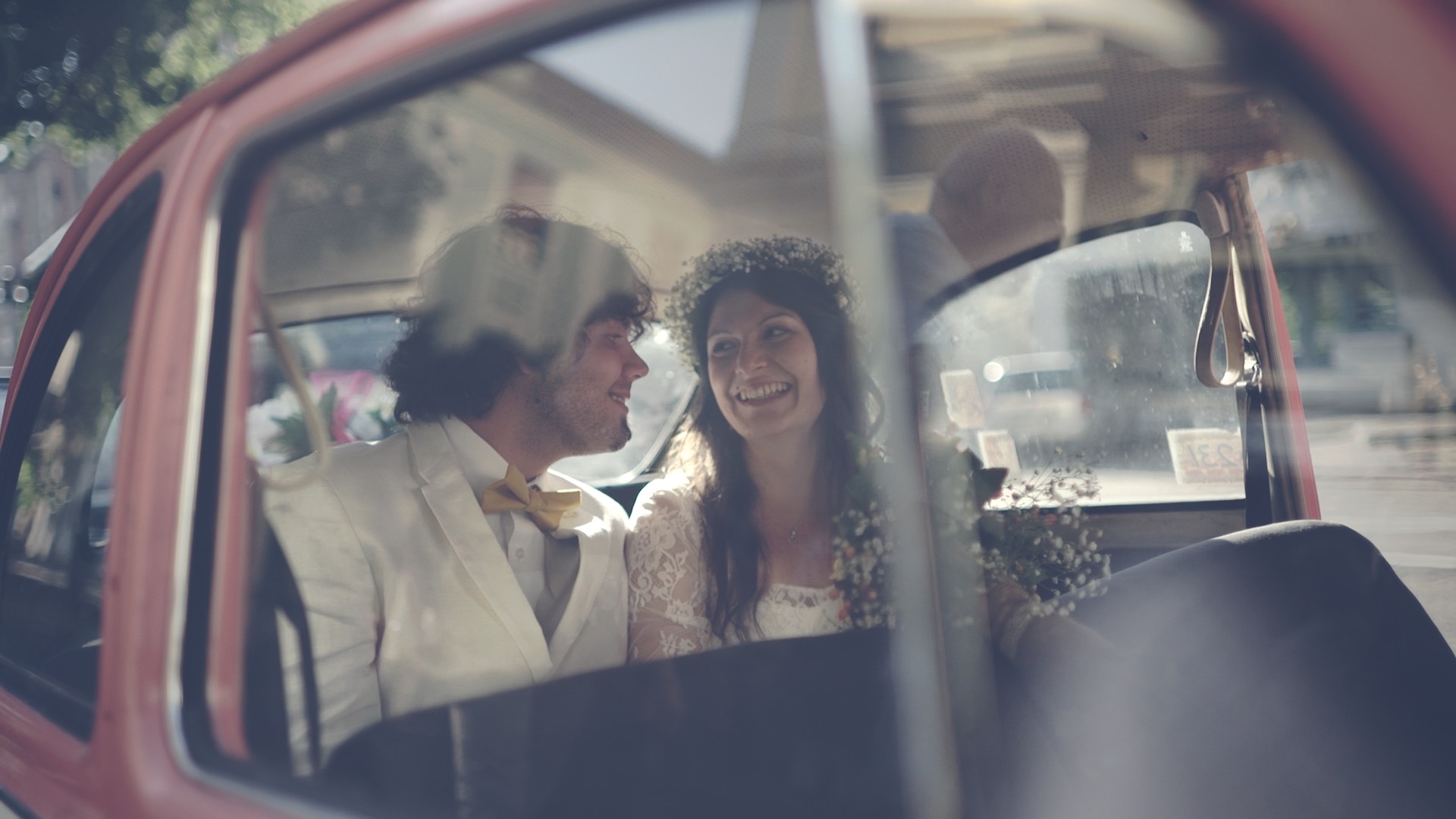 Asy és Zsuska mosolyognak és egymásra néznek az esküvői autó ablakán keresztül – vintage vörös autó Vekeri tó mellett